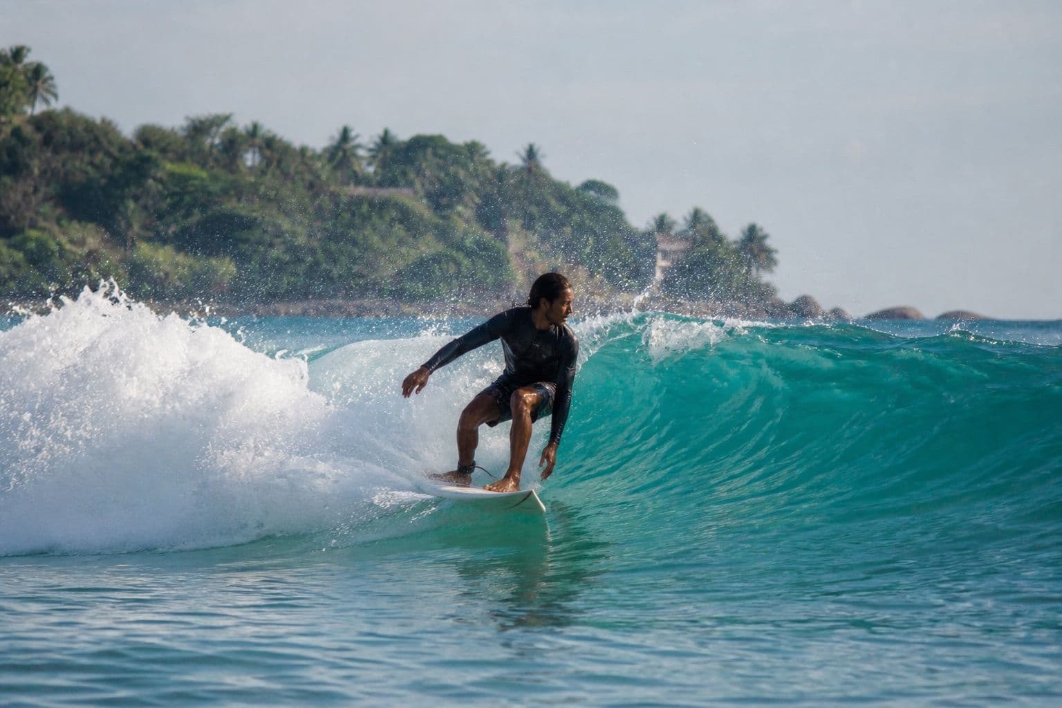 Surfer riding a turquoise wave on Sri Lanka’s coast